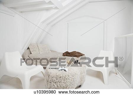 Stock Image - Chess board and video game controller on ottoman with chairs and sofa in room. Fotosearch