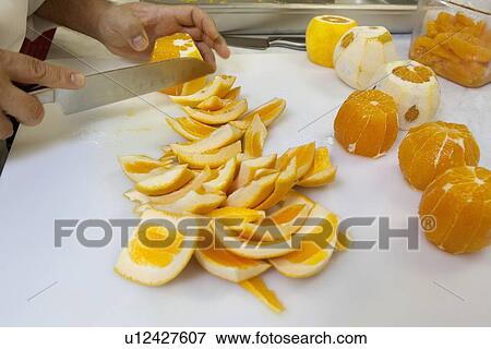 Stock Photo - Close-up of hands slicing oranges with knife. Fotosearch