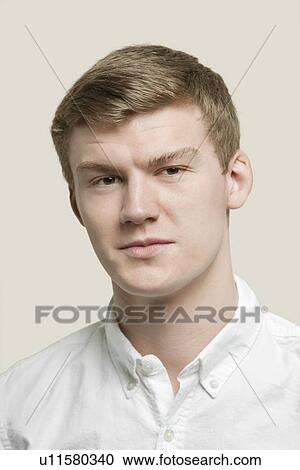 Stock Image - Close-up portrait of serious young man against gray background. Fotosearch
