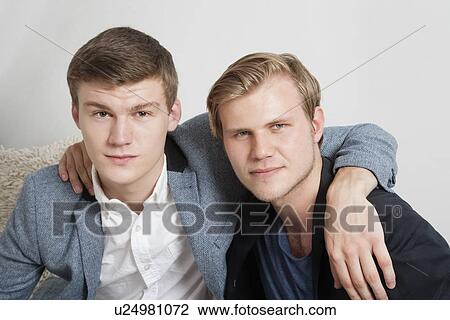 Stock Image - Close-up portrait of two young male friends with arms around. Fotosearch