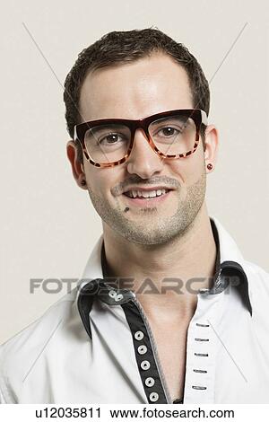 Stock Image - Close-up portrait of young man wearing eyeglasses against gray background. Fotosearch