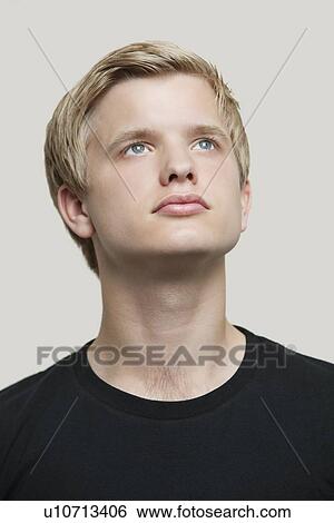Stock Photograph - Contemplative young man looking up against gray background. Fotosearch