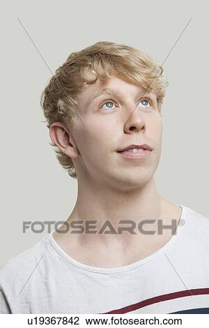 Stock Image - Contemplative young man standing against gray background. Fotosearch