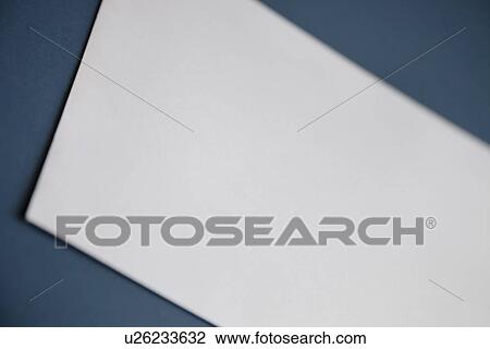 Stock Image - Cropped image of a blank white paper on dark blue surface. Fotosearch