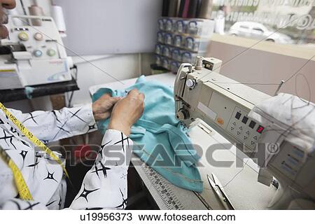 Stock Image - Cropped image of male tailor stitching cloth while sitting by sewing machine. Fotosearch