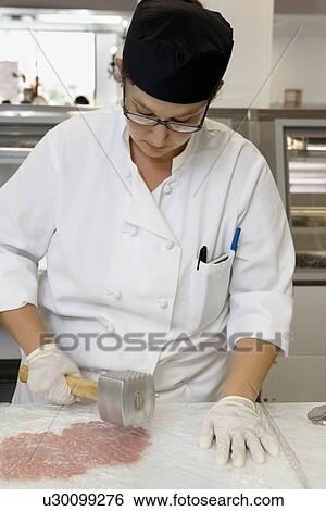 Stock Photograph - Female chef tenderizing meat with meat hammer. Fotosearch