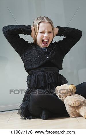 Frustrated young girl covering ears and screaming while sitting on floor View Large Photo Image Stock Photo - Frustrated young girl covering ears and screaming while sitting on floor. Fotosearch