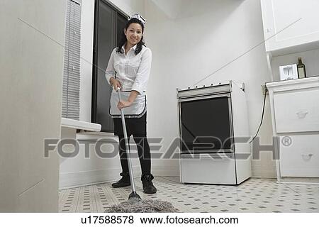 Stock Photo - Full length portrait of young housemaid cleaning floor with mop. Fotosearch