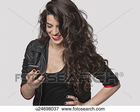 Happy young female using cell phone against gray background View Large Photo Image Stock Photo - Happy young female using cell phone against gray background. Fotosearch