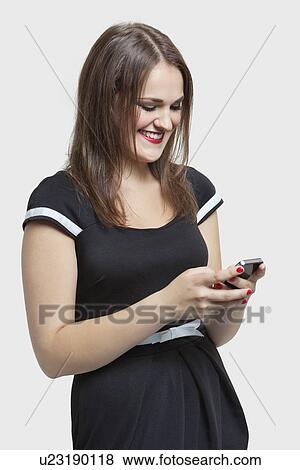 Happy young woman text messaging through cell phone over gray background View Large Photo Image Stock Photo - Happy young woman text messaging through cell phone over gray background. Fotosearch