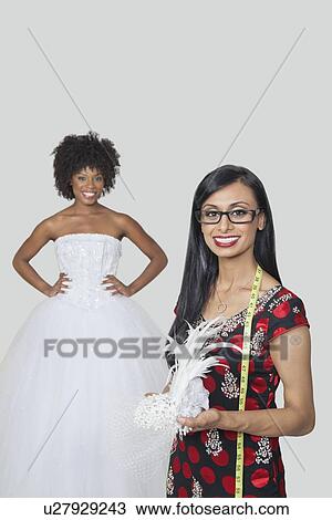 Indian female fashion designer holding feather fascinator with African American bride standing against gray background View Large Photo Image Stock Image - Indian female fashion designer holding feather fascinator with African American bride standing against gray background. Fotosearch