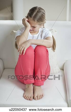 Stock Photo - Little girl crying while sitting on sofa. Fotosearch