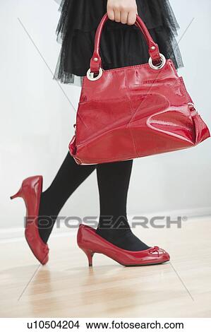 Picture - Low section of girl wearing a woman's high heels while carrying red handbag. Fotosearch