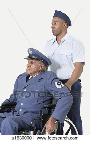 Stock Image - Male cadet assisting senior air force officer in wheelchair over light gray background. Fotosearch