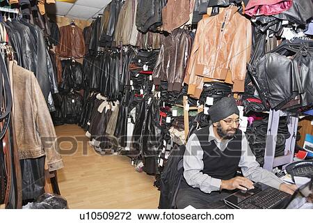 Stock Image - Man working on laptop at clothing shop. Fotosearch