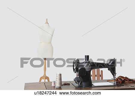 Picture - Mannequin and sewing machine with threads over gray background. Fotosearch