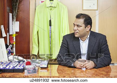 Mid adult male salesperson sitting at desk in menswear store View Large Photo Image Stock Image - Mid adult male salesperson sitting at desk in menswear store. Fotosearch
