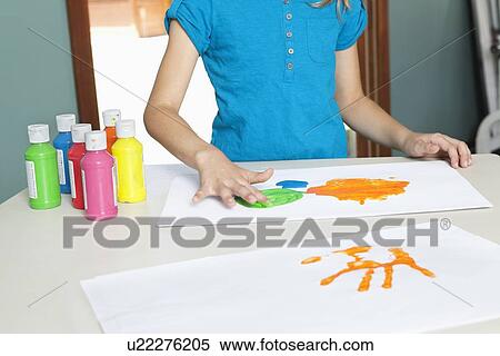 Stock Photography - Mid section of a young girl finger painting on paper at table. Fotosearch