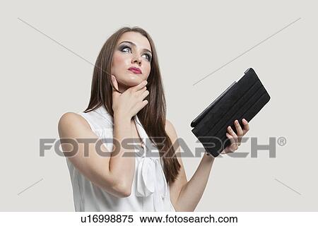 Pensive young woman holding tablet PC over gray background View Large Photo Image Stock Photography - Pensive young woman holding tablet PC over gray background. Fotosearch