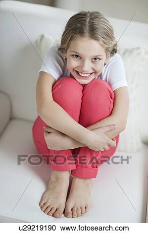 Stock Image - Portrait of a happy young girl sitting on sofa. Fotosearch