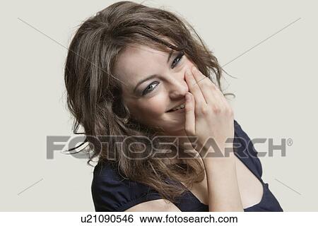 Portrait of a woman smiling with hand over mouth against gray background View Large Photo Image Stock Photograph - Portrait of a woman smiling with hand over mouth against gray background. Fotosearch