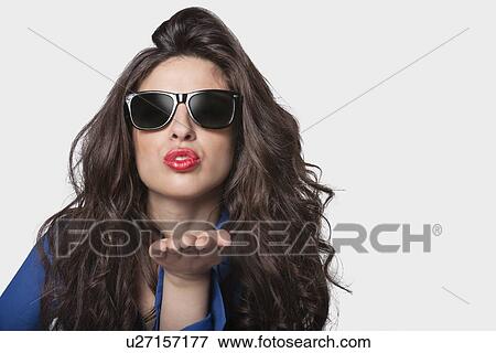 Stock Photo - Portrait of a young woman in sunglasses blowing a kiss over gray background. Fotosearch