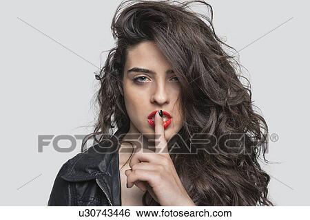 Portrait of a young woman with unkept hair and finger on lips against gray background View Large Photo Image Stock Photograph - Portrait of a young woman with unkept hair and finger on lips against gray background. Fotosearch