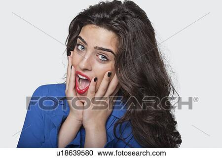 Stock Image - Portrait of an amazed young woman over gray background. Fotosearch