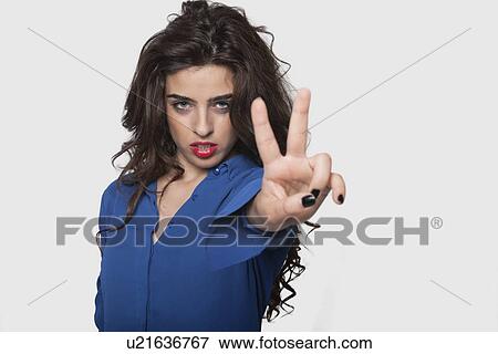 Portrait of an arrogant young woman gesturing victory sign against gray background View Large Photo Image Stock Photo - Portrait of an arrogant young woman gesturing victory sign against gray background. Fotosearch