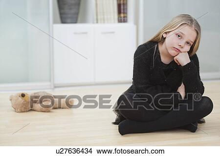 Picture - Portrait of an upset girl sitting on hardwood floor by stuffed toy. Fotosearch