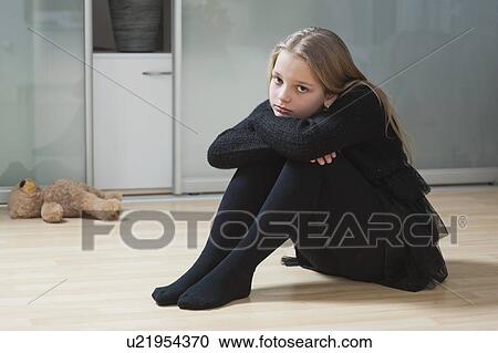 Stock Image - Portrait of an upset girl sitting on hardwood floor. Fotosearch
