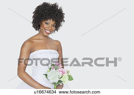 Picture - Portrait of beautiful African American bride holding bouquet over gray background. Fotosearch