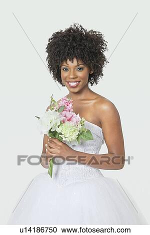Stock Image - Portrait of beautiful African American bride holding bouquet over gray background. Fotosearch