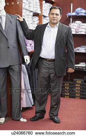 Stock Image - Portrait of businessman standing by mannequin dressed in suit at menswear store. Fotosearch