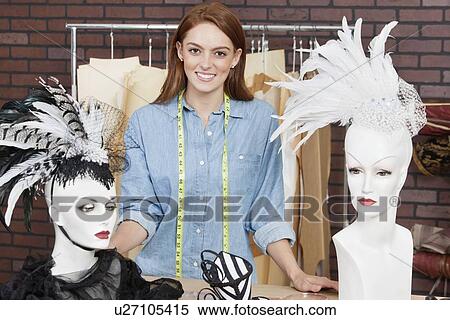 Stock Photography - Portrait of female fashion designer standing by table with fascinators on mannequin. Fotosearch