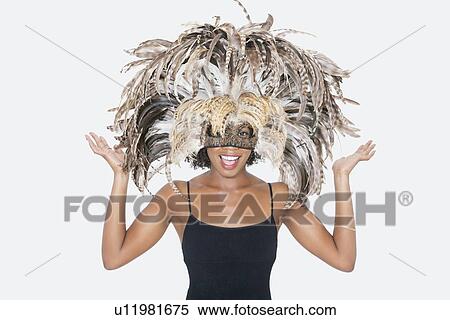 Stock Photography - Portrait of happy African American woman wearing a feather mask over gray background. Fotosearch