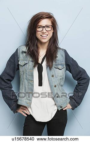 Portrait of happy young woman with hands on hip standing against light blue background View Large Photo Image Stock Image - Portrait of happy young woman with hands on hip standing against light blue background. Fotosearch
