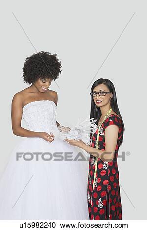 Portrait of Indian female designer assisting African American bride with feather fascinator over gray background View Large Photo Image Stock Image - Portrait of Indian female designer assisting African American bride with feather fascinator over gray background. Fotosearch