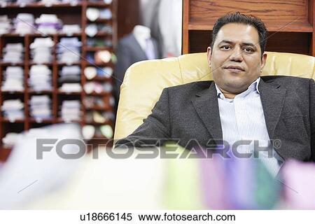 Stock Photography - Portrait of mature male owner sitting on chair. Fotosearch