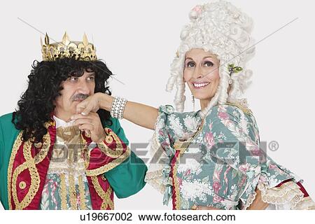Stock Image - Portrait of queen smiling as the king kisses her hand over gray background. Fotosearch