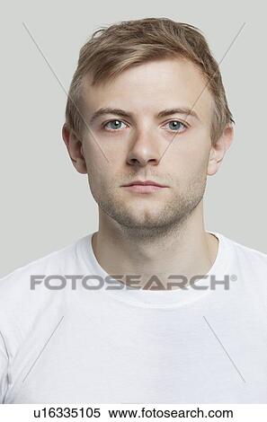 Stock Photography - Portrait of serious young man in t-shirt against gray background. Fotosearch