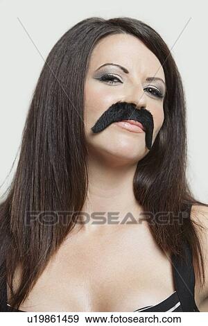 Stock Photo - Portrait of serious young woman with fake mustache against gray background. Fotosearch