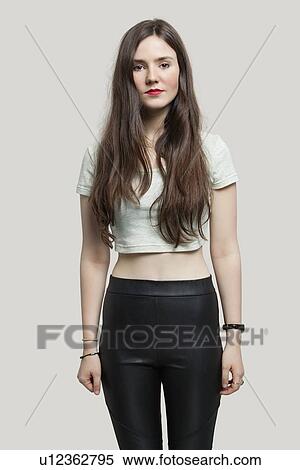 Stock Photography - Portrait of serious young woman with long brunette hair standing against gray background. Fotosearch