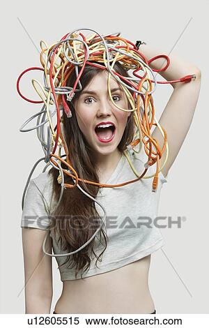 Stock Photography - Portrait of shocked young woman's head tangled with colorful cables over gray background. Fotosearch