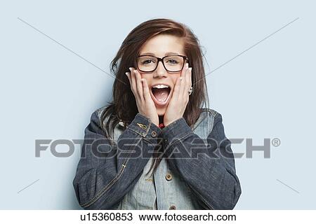 Portrait of surprised young woman with hands on cheeks against light blue background View Large Photo Image Stock Image - Portrait of surprised young woman with hands on cheeks against light blue background. Fotosearch