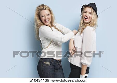 Portrait of two playful young women sticking out tongues against light blue background View Large Photo Image Stock Photo - Portrait of two playful young women sticking out tongues against light blue background. Fotosearch