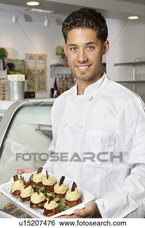 Stock Photograph - Portrait of young male chef holding dessert in serving dish. Fotosearch