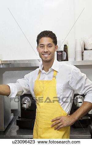 Stock Image - Portrait of young male waiter standing with hand on hip. Fotosearch