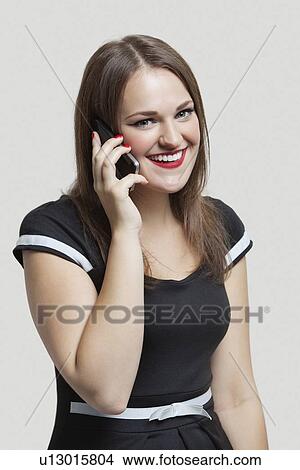 Picture - Portrait of young woman communicating on cell phone over gray background. Fotosearch