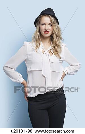 Stock Photo - Portrait of young woman in smart casuals with hands on hip against light blue background. Fotosearch
